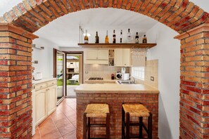 A kitchen with a brick archway, a bar area with stools, and a variety of bottles on the shelf. - Apartment 'Claire' with Private Garden (San Giovanni Suergiu)