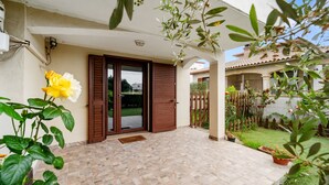 Un patio techado con suelo de baldosas, una puerta de madera y un pequeño jardín con plantas en macetas.