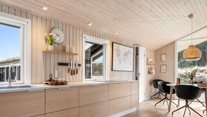 Una cocina moderna con muebles de madera, un ventanal grande y una zona de comedor con sillas negras y una mesa.
