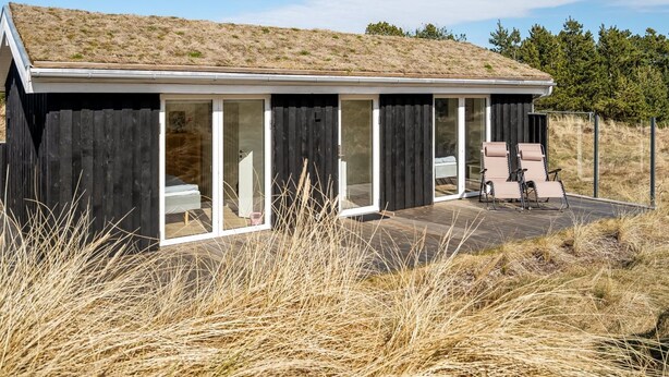 Una casa moderna con techo plano, grandes puertas correderas de vidrio y un patio con mobiliario exterior.