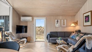 Una habitación acogedora con techo de madera, un sofá gris, un televisor y una chimenea.