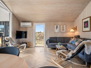 Ein gemütliches Zimmer mit Holzbalkendecke, einem grauen Sofa, einem Fernseher und einem Kamin.