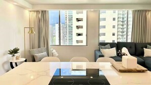 Uma sala de estar moderna com área de jantar, janelas amplas, um sofá e uma mesa com fogão por indução embutido.