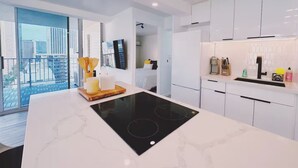 Cozinha moderna com armários brancos, fogão por indução preto e uma janela grande com vista para a cidade.