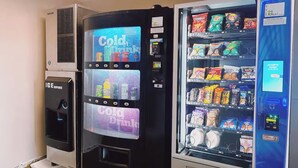 Máquina automática com sinal 'Bebidas Geladas', um dispensador de bebidas geladas e variedade de snacks e bebidas no interior.