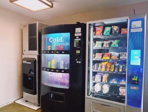 Ein Getränkeautomat mit einem Schild für 'Cold Drinks', einem Kaltgetränkeausgabefeld und einer Auswahl an Snacks und Getränken.