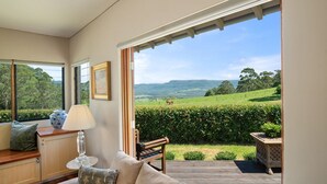 A room with a large window, a wooden bench, a table with a lamp, and a framed picture on the wall. - Newhaven - Kangaroo Valley (Upper Kangaroo River)