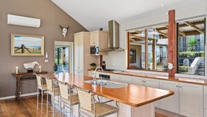 A kitchen with a central island, wooden cabinets, a microwave, and a large window with a view. - Newhaven - Kangaroo Valley (Upper Kangaroo River)