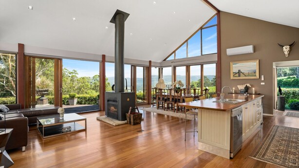 A spacious living area with a fireplace, dining table, and large windows offering a view of the outdoors. - Newhaven - Kangaroo Valley (Upper Kangaroo River)