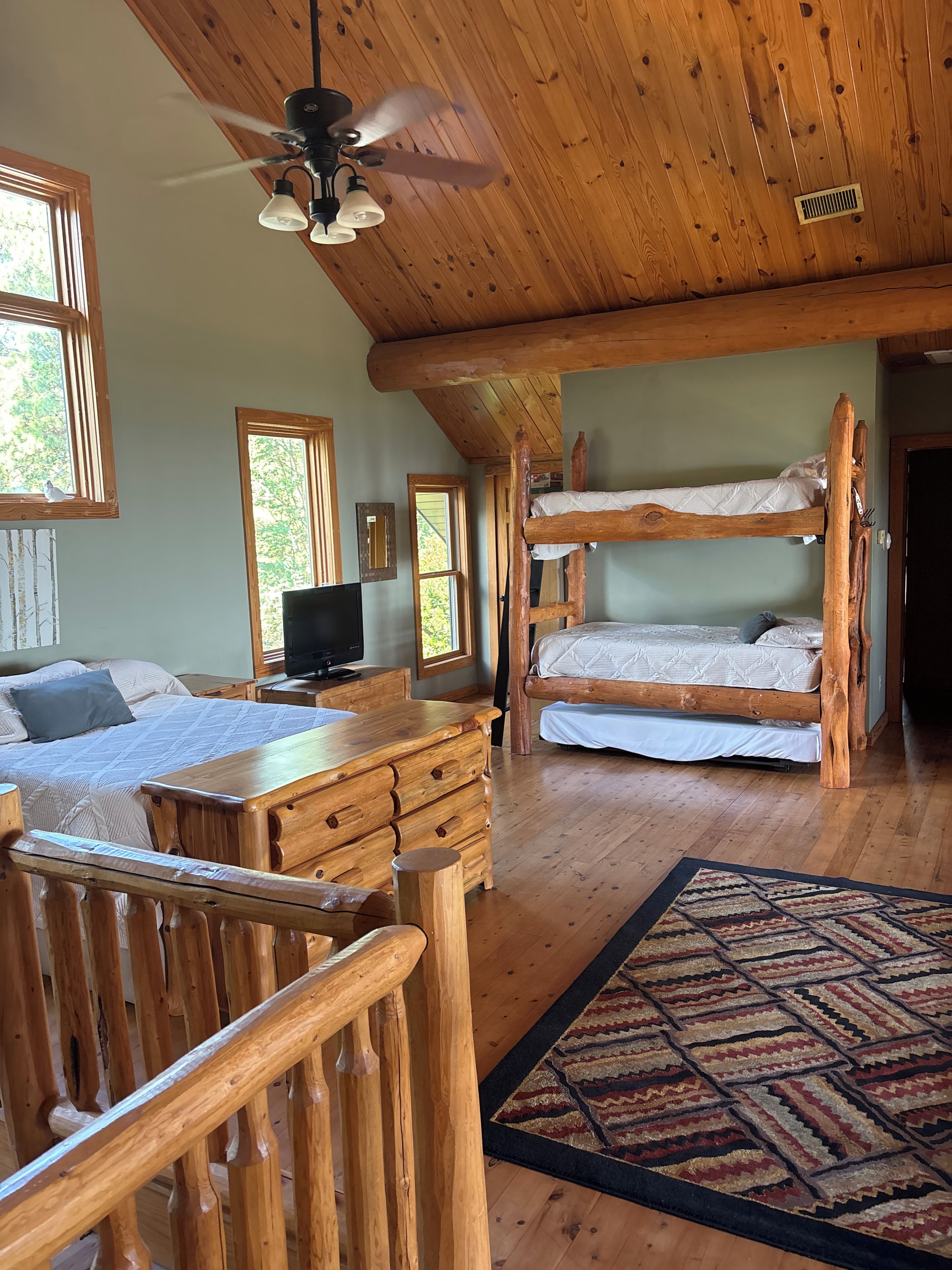 A cabin interior with a bunk bed, wooden furniture, a ceiling fan, and a television.
