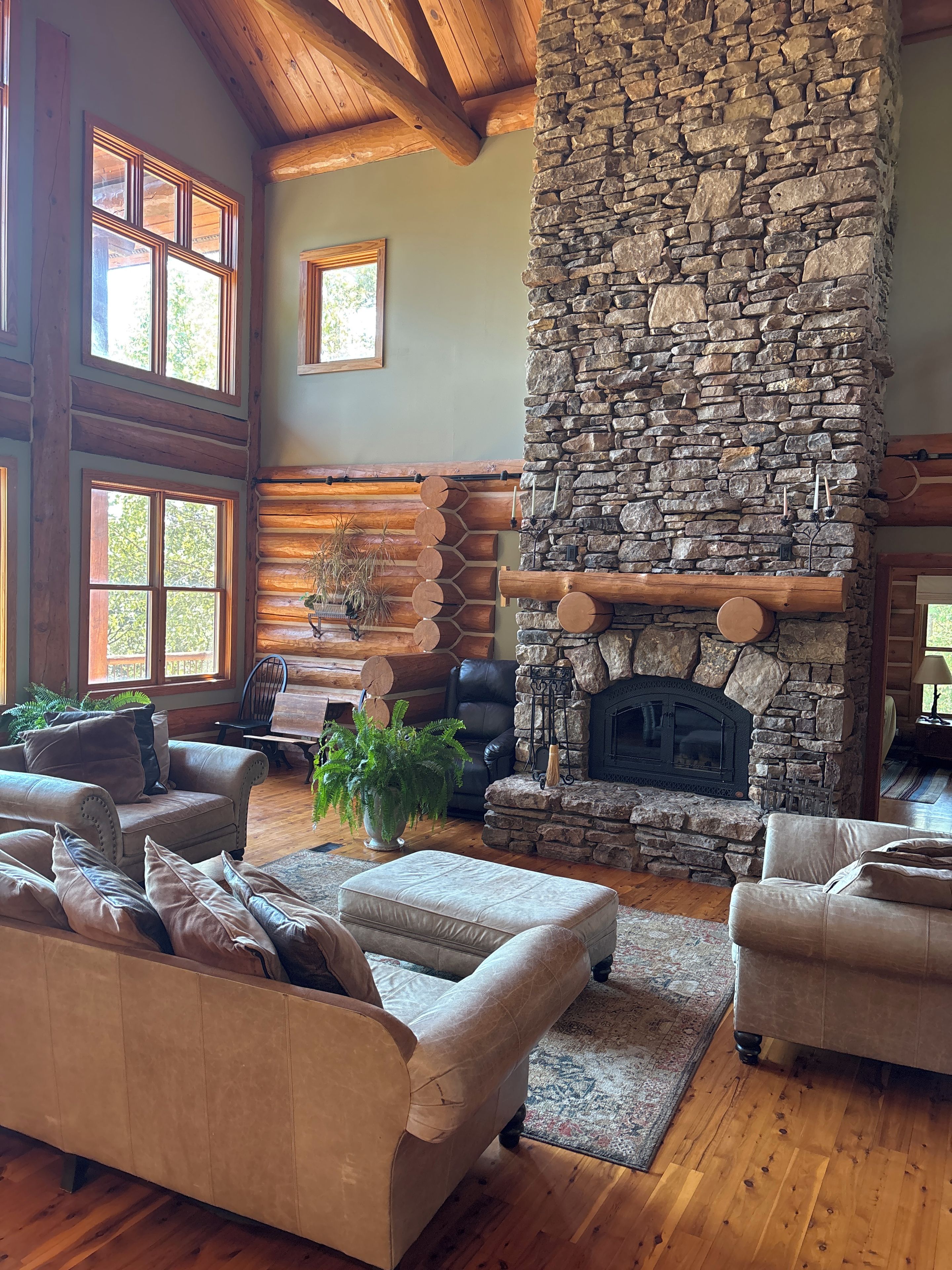 A cozy living room with a stone fireplace, leather sofas, and a wooden ceiling.