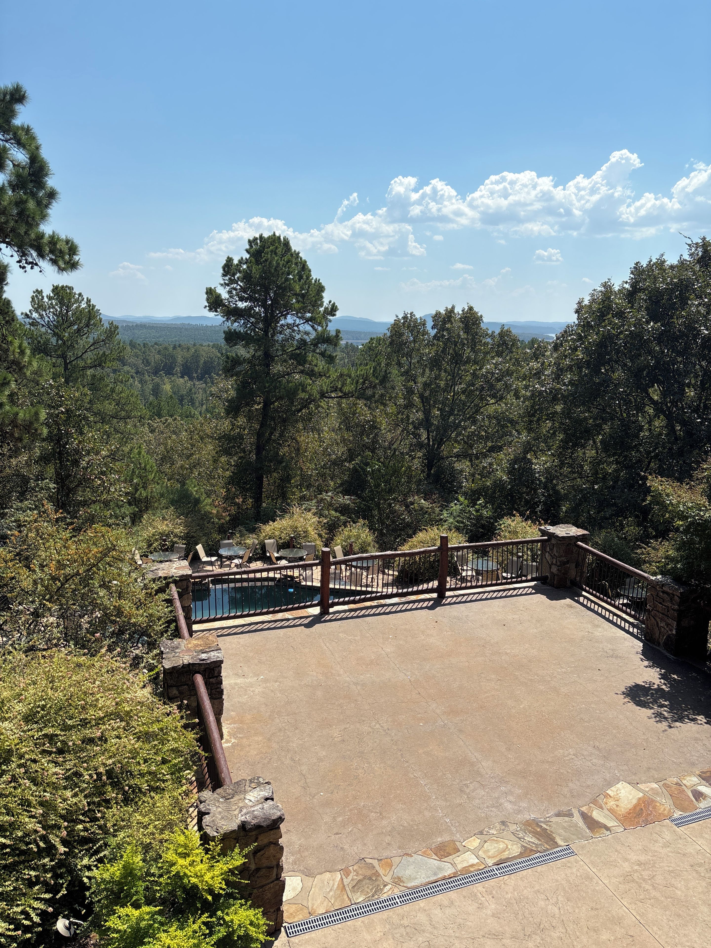 A pool area with a stone deck, surrounded by trees and a stone railing.