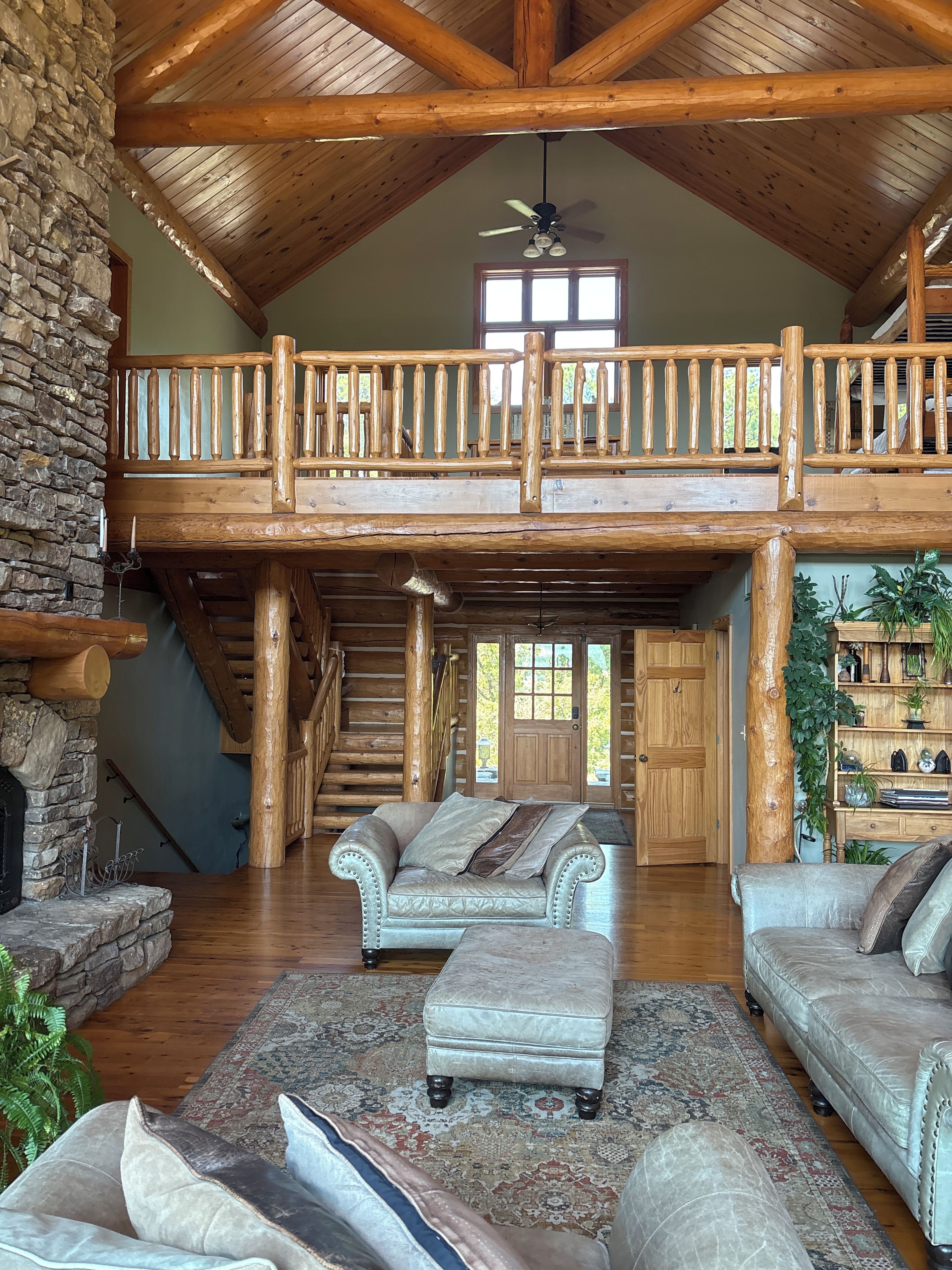 A spacious interior with a high ceiling, a stone fireplace, a wooden staircase, and a balcony with a railing.