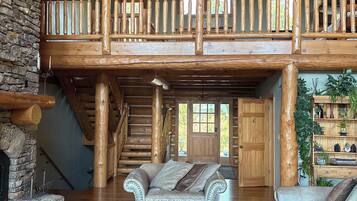 A spacious interior with a high ceiling, a stone fireplace, a wooden staircase, and a balcony with a railing.