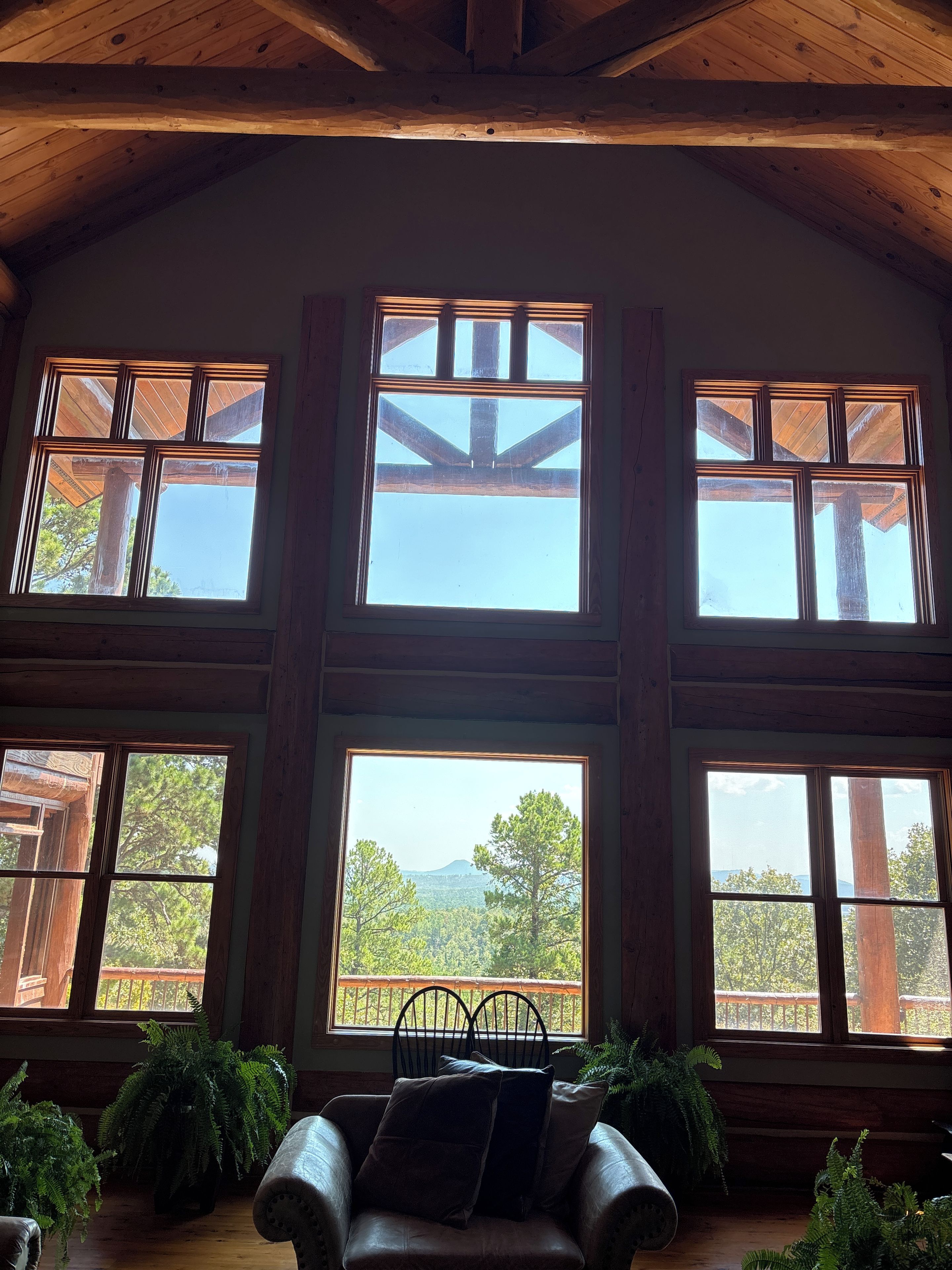 A room with large windows, wooden beams, and a view of trees and mountains.
