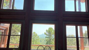 A room with large windows, wooden beams, and a view of trees and mountains.