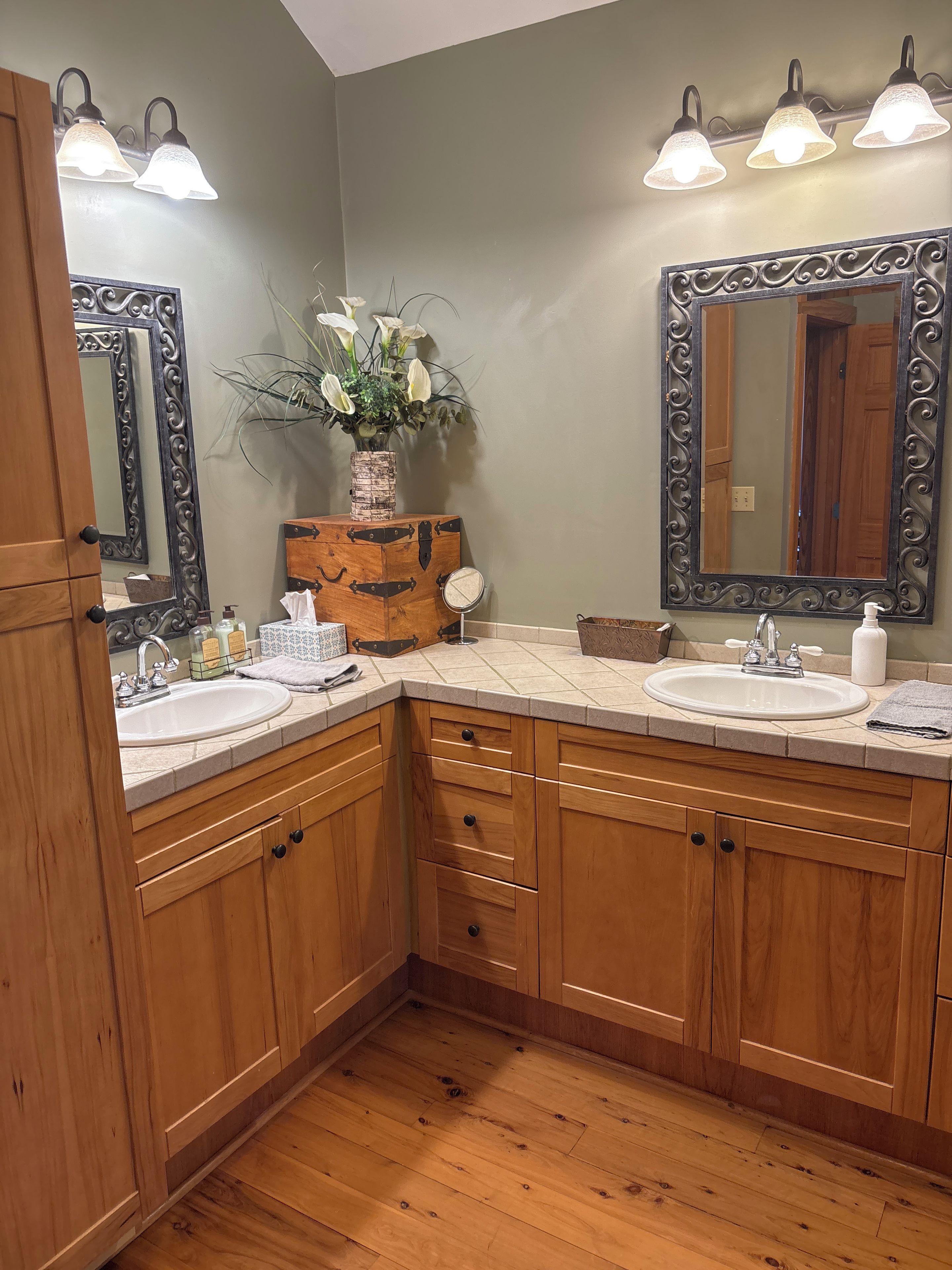 A bathroom with wooden cabinets, a sink, a mirror, and a vase with flowers.