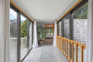A corridor with large sliding glass doors leading to a balcony, a potted plant, and a bed with a view of the outdoors.