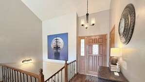 Una escalera con barandilla de madera, un candelabro, una puerta con paneles de vidrio y un plato decorativo en la pared.