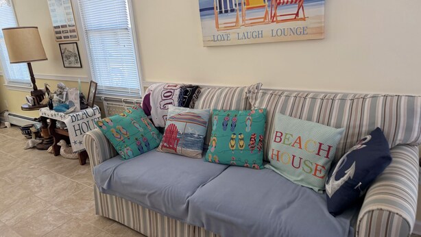 Ein gestreiftes Sofa mit Strandkissen, ein Schild mit der Aufschrift 'Beach House' und ein Schild mit der Aufschrift 'Love Laugh Lounge' an der Wand.