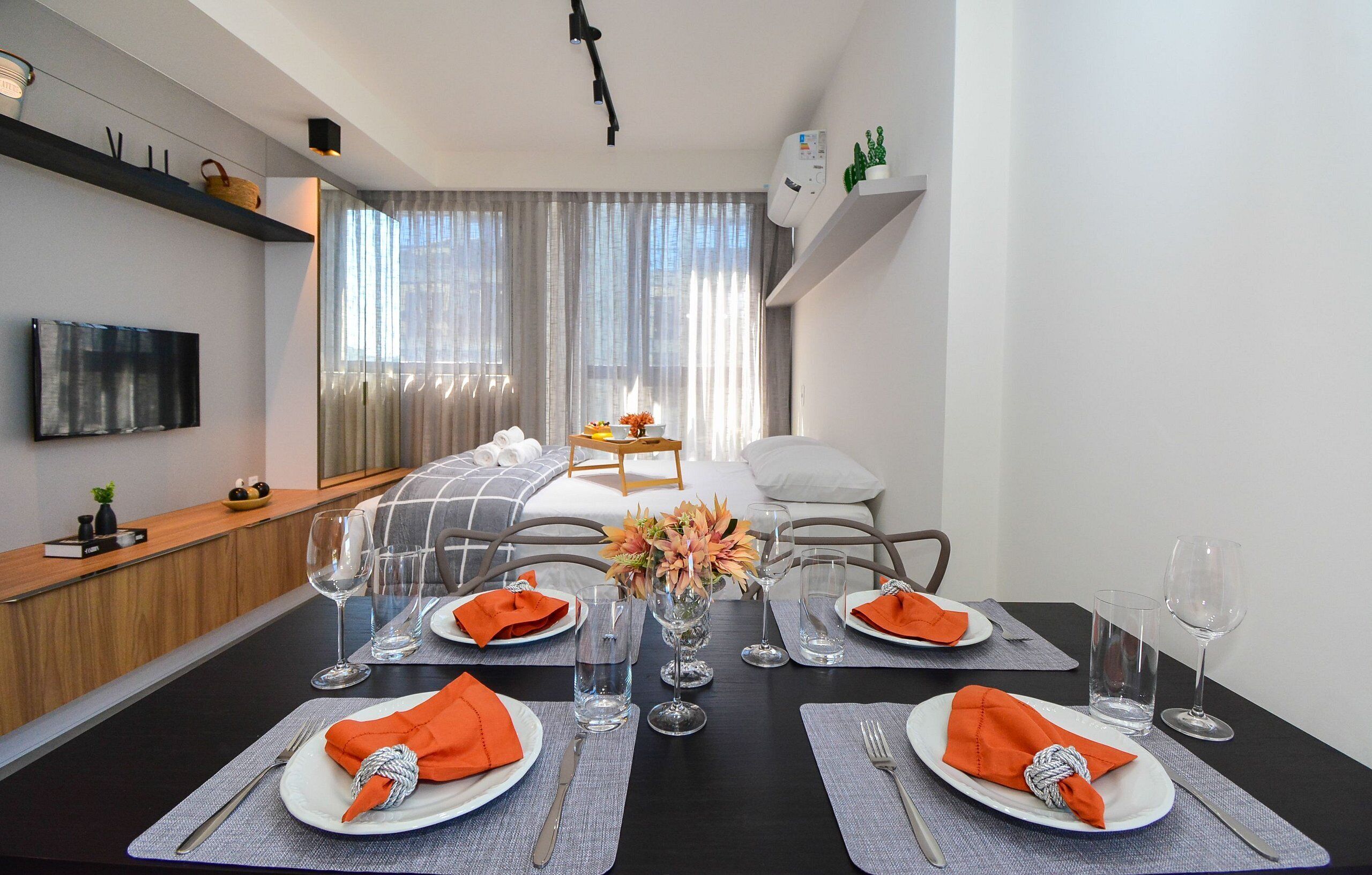 Un comedor moderno con una mesa negra, platos blancos y servilletas naranja.