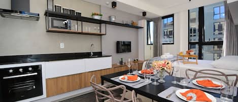 Une cuisine moderne dotée d’appareils électroménagers intégrés, un coin repas avec une table dressée pour deux personnes et une grande fenêtre laissant entrer la lumière naturelle.