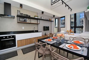 Una cocina moderna con electrodomésticos integrados, un comedor con una mesa dispuesta para dos personas y un amplio ventanal que proporciona luz natural.