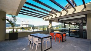 An outdoor terrace with a table and chairs, a potted plant, and a view of the cityscape. - Studio em frente a UFSC e HU - 625A (Florianópolis)