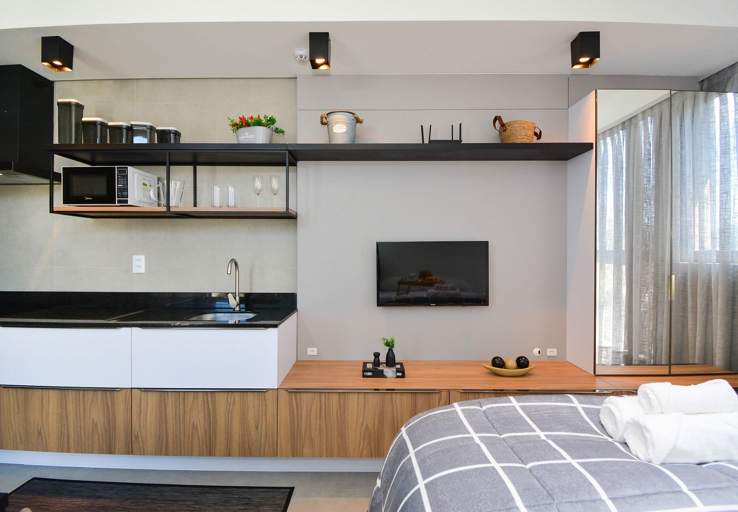 A modern kitchen with built-in appliances, a dining area with a flat-screen TV, and a bedroom with a large bed and a view of the city.
