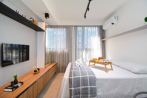 A modern hotel room with a bed, bedside table, TV, and a window with curtains. - Studio em frente a UFSC e HU - 625A (Florianópolis)