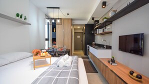 A modern hotel room with a bed, bedside table, TV, and kitchenette. - Studio em frente a UFSC e HU - 625A (Florianópolis)