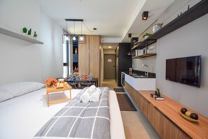 A modern hotel room with a bed, bedside table, TV, and kitchenette. - Studio em frente a UFSC e HU - 625A (Florianópolis)