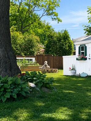 Patio trasero cercado con una estatua de perro, una terraza de madera y un edificio blanco con un cartel de 'Welcome'.