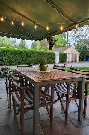 Eine Terrasse im Freien mit einem Holztisch und gestreiften Stühlen, überdacht und mit Lichterketten geschmückt.