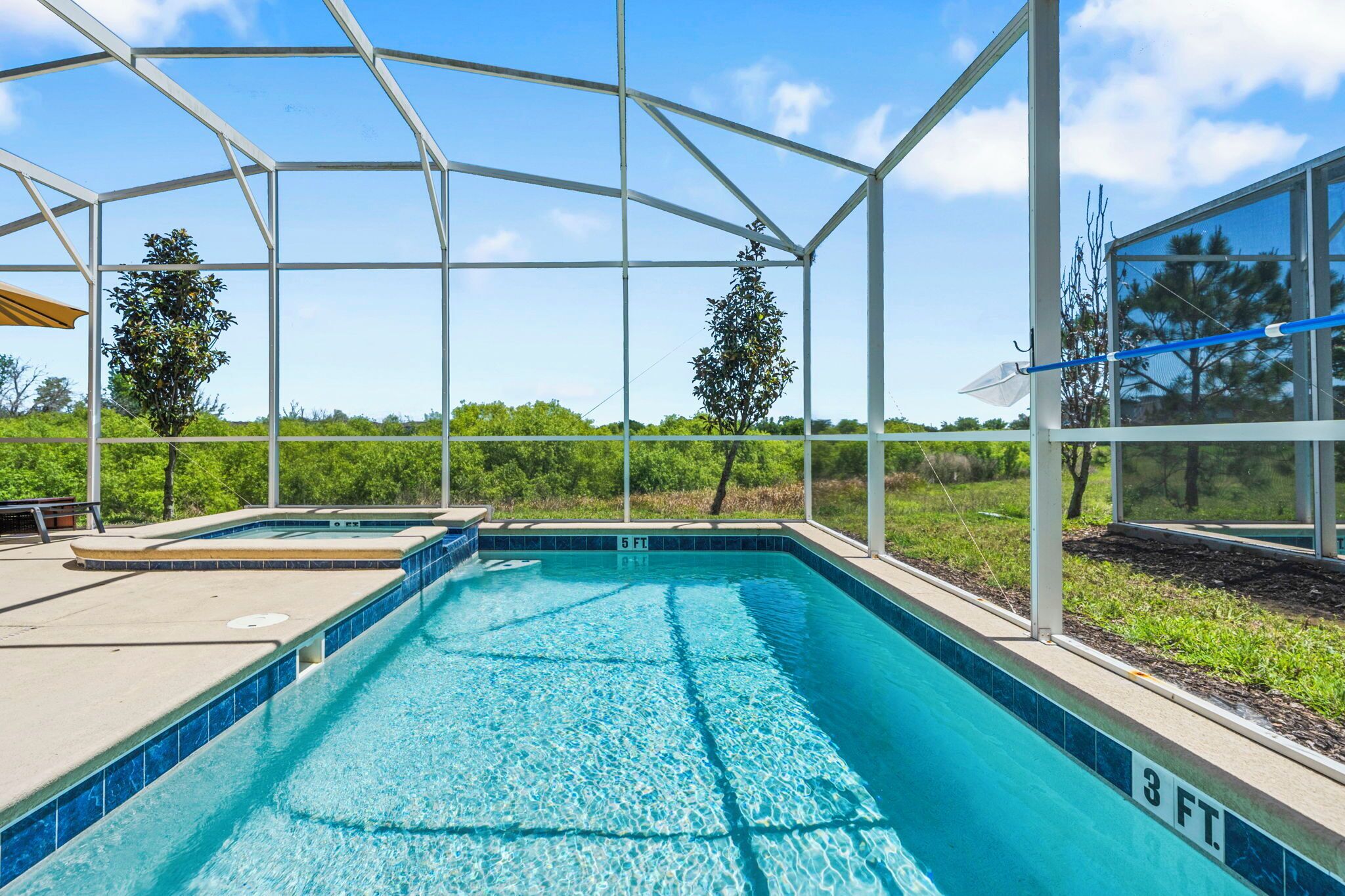 Une piscine dotée d’une zone couverte, entourée de verdure et surplombée par un ciel dégagé.