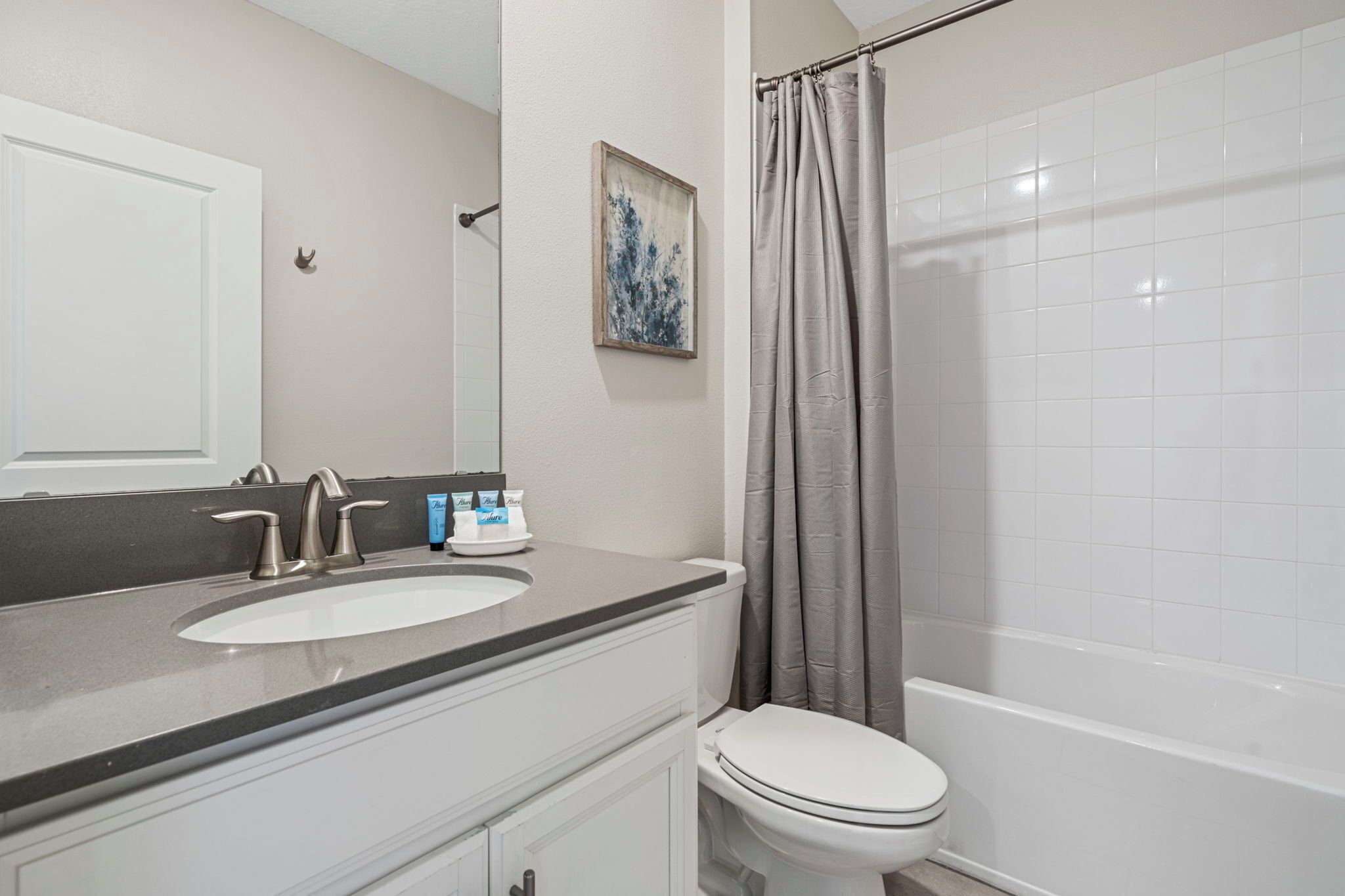 Un baño con un lavabo blanco, un inodoro, una cortina de ducha y un cuadro en la pared.