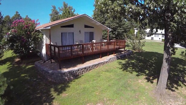 Una casa de un solo piso con un porche, cimientos de piedra y un patio cubierto de césped.