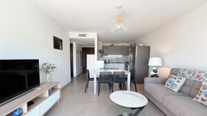 A modern living room with a flat-screen TV, a glass coffee table, a sofa with floral cushions, and a kitchen in the background. - T2 Porticcio sea view beach on foot (Grosseto-Prugna)