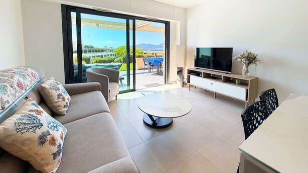 A modern living room with a sofa, coffee table, TV, and a balcony with outdoor furniture. - T2 Porticcio sea view beach on foot (Grosseto-Prugna)