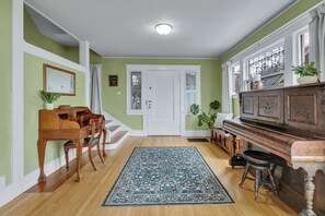 Una habitación con un piano, una mesa de comedor con sillas, una escalera y un tapete grande.