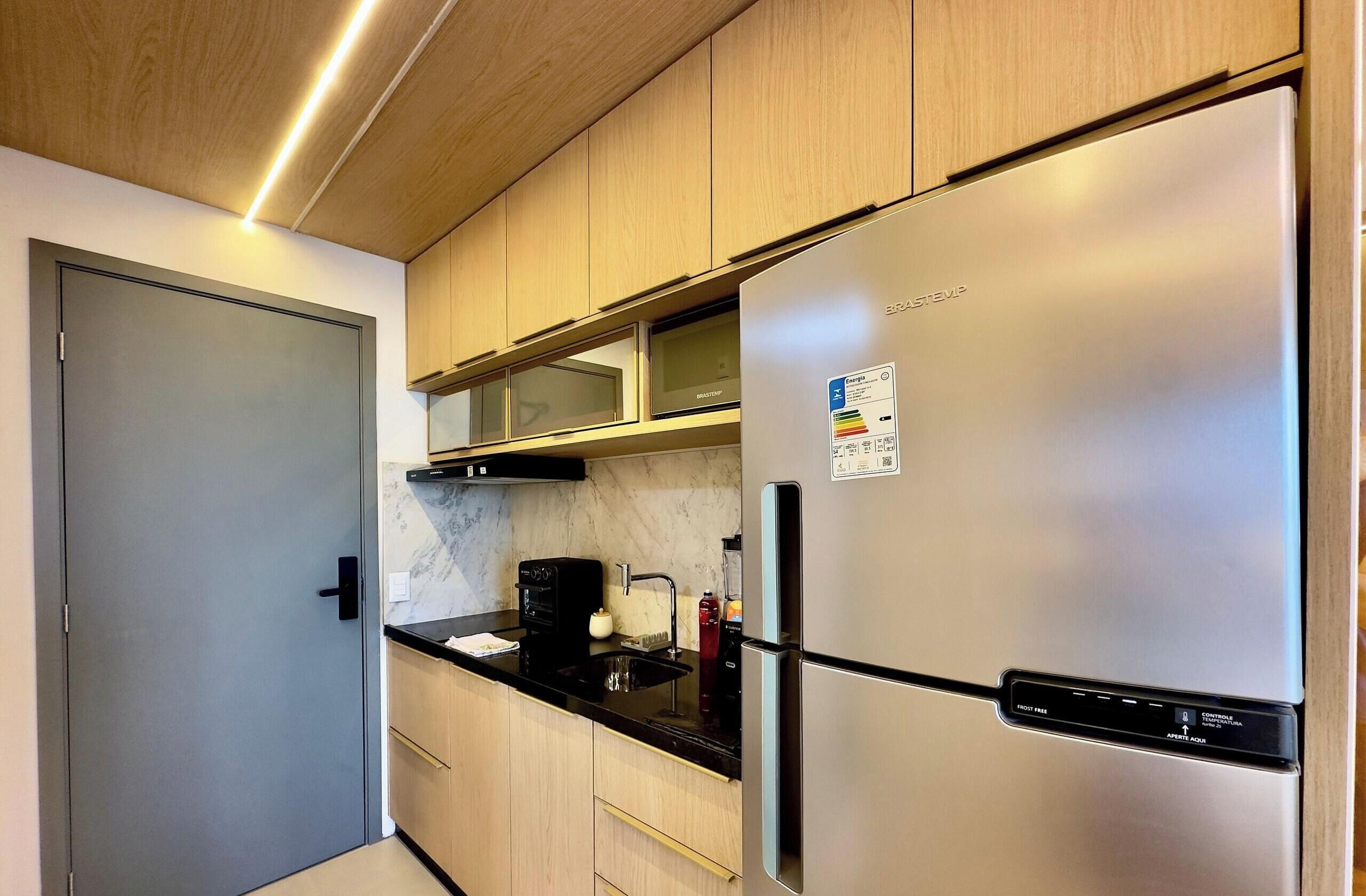 Una cocina moderna con un refrigerador de acero inoxidable, gabinetes de madera, una encimera negra y un microondas integrado.