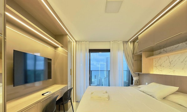 A modern hotel room with a large bed, a TV, a desk, and a view of the cityscape. - Beach Class Meireles (Fortaleza)
