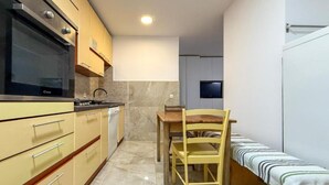 A compact kitchen with a built-in oven, a dining table with chairs, and a small television mounted on the wall. - Capo & Nemo Apartments Vodice - Classic One Bedroom Apartment (Vodice)