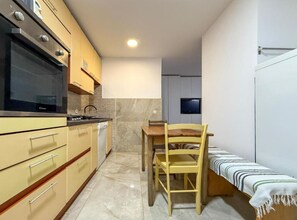 Eine kompakte Küche mit eingebautem Backofen, einem Esstisch mit Stühlen und einem kleinen, an der Wand befestigten Fernseher.
