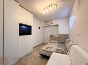 Ein kleines, modernes Schlafzimmer mit Bett, Fernseher und Fenster mit Jalousien.