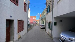 A narrow street with buildings on either side, a car parked on the right, and a clear blue sky. - Capo & Nemo Apartments Vodice - Classic One Bedroom Apartment (Vodice)