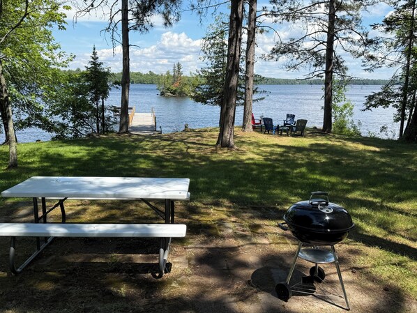 Ein Picknickplatz mit Grill, Bank und Stühlen am See.