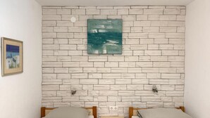 Una habitación con dos camas individuales, una mesita de noche de madera, un cuadro colgado en la pared y una foto enmarcada a la izquierda.