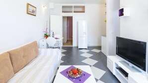 Una sala de estar moderna con un sofá, un televisor, un comedor con una mesa y sillas, y una cocina con un refrigerador.