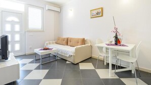 Una sala de estar con un sofá, una mesa de comedor con sillas, un televisor y un marco de fotos en la pared.